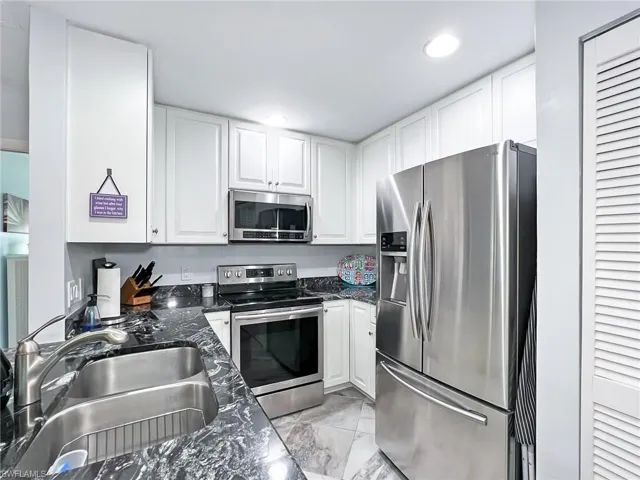 Kitchen with dark stone countertops, white cabinetry, stainless steel appliances, and sink