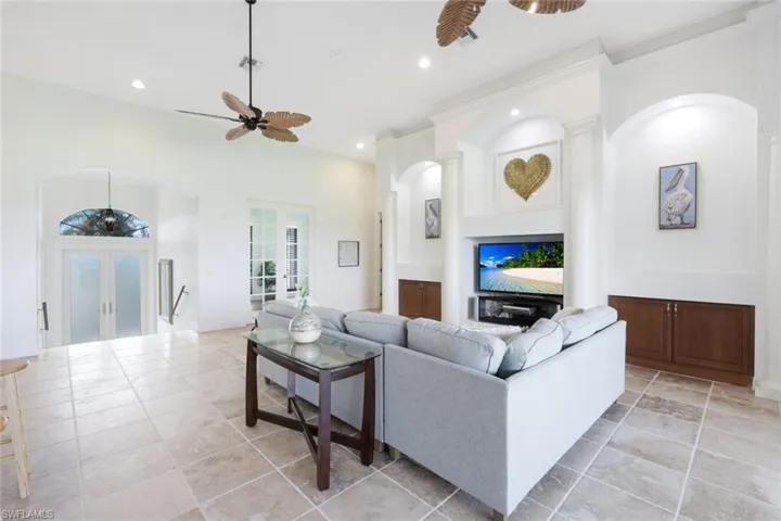 Living room featuring ceiling fan, french doors, ornate columns, and light tile patterned floors