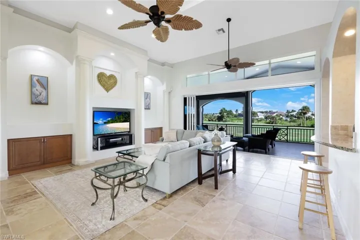 Living room featuring ceiling fan, light tile patterned flooring, a towering ceiling, and ornate columns