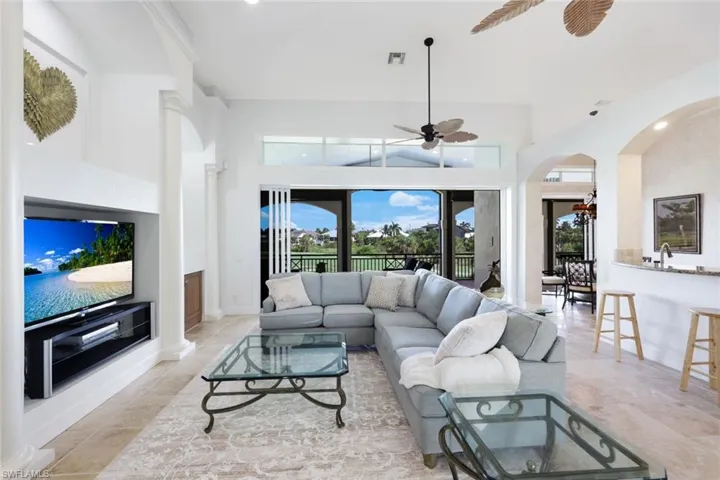 Living room featuring ceiling fan, a high ceiling, light tile patterned floors, decorative columns, and sink