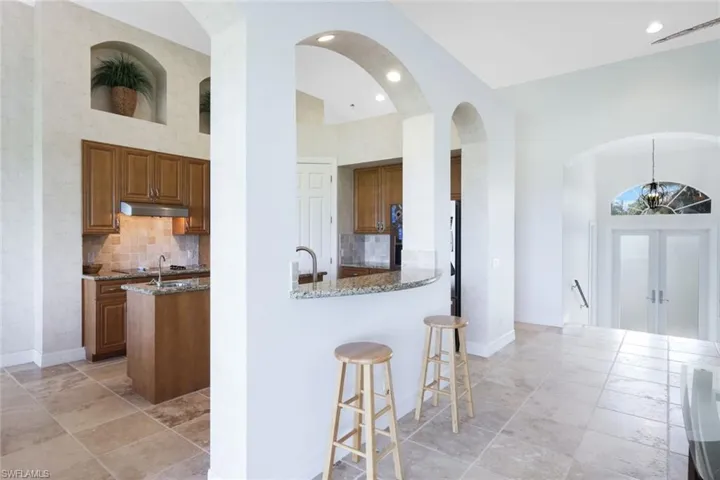 Kitchen featuring high vaulted ceiling, backsplash, light tile patterned flooring, dark stone counters, and kitchen peninsula