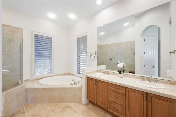 Bathroom with double sink vanity, shower with separate bathtub, tile patterned floors, and lofted ceiling