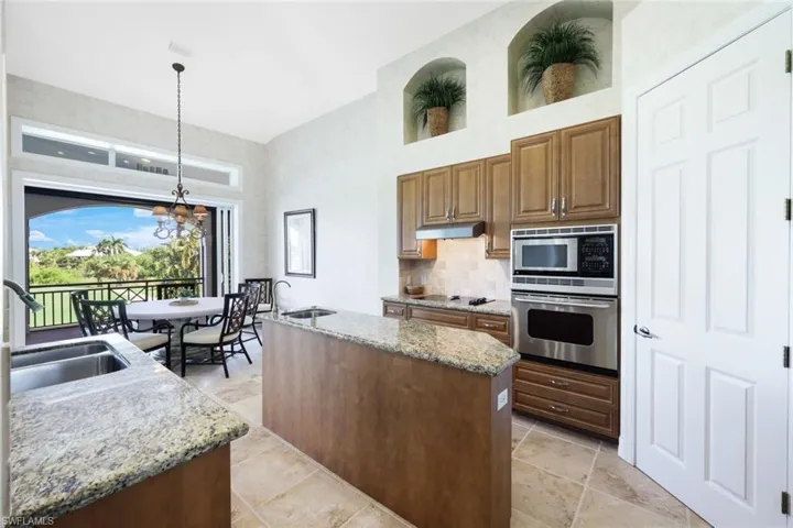 Kitchen with a center island with sink, stainless steel appliances, hanging light fixtures, light stone counters, and a chandelier