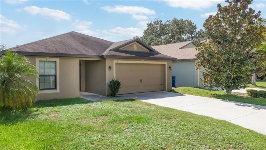 Single-story stucco exterior featuring a gabled roofline, two-car garage, concrete driveway, and landscaped lawn