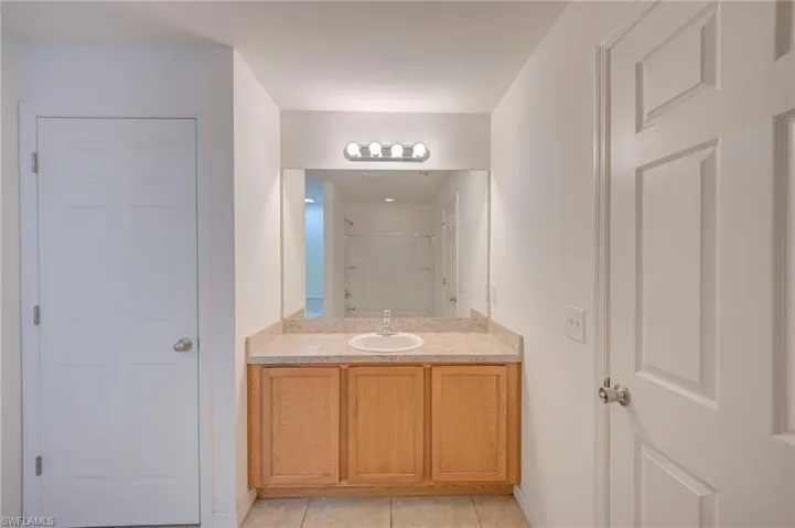 Bathroom vanity with wood-finish cabinetry, stone-composite countertop, integrated sink, wall-to-wall vanity mirror, and four-light overhead fixture