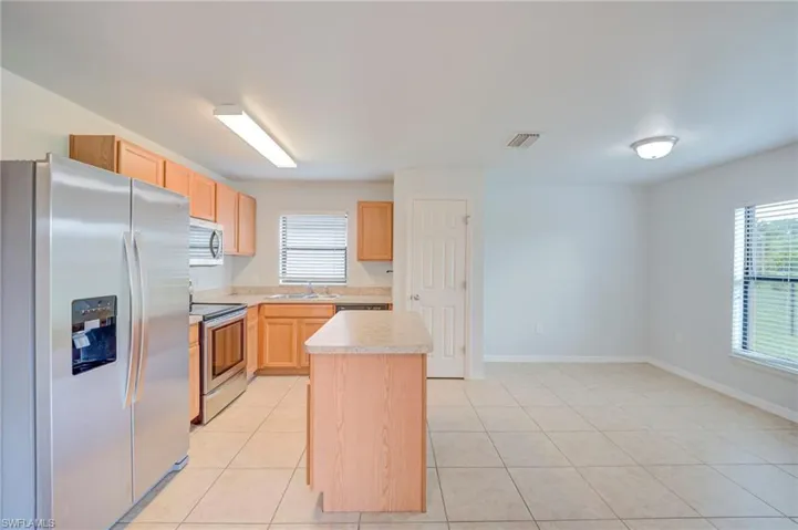 Kitchen featuring light wood-finish cabinetry, stone-texture countertops, a center island, stainless steel refrigerator and range, and tiled flooring