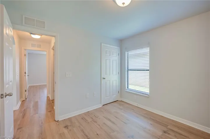 Room featuring wood-finish flooring, a six-panel door, neutral wall paint, and a window with integrated blinds