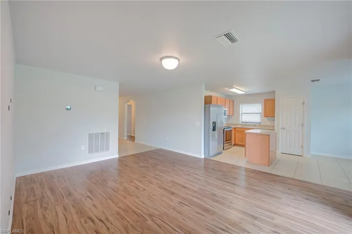 Open-concept interior featuring wood-finish flooring, tile kitchen flooring, light wood cabinetry, stainless steel refrigerator, and central kitchen island