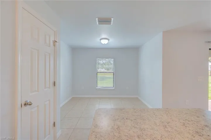 Neutral-toned interior space featuring ceramic tile flooring, a single-pane window with horizontal blinds, a six-panel interior door, and a flush-mount ceiling light fixture