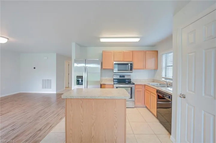 Kitchen featuring a central island with a stone-finish countertop, light-wood cabinetry, stainless steel appliances, and tile flooring