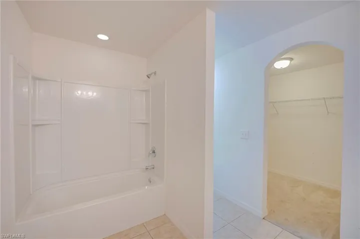 Full bathroom featuring a tub-shower combination with integrated shelving, recessed lighting, tile flooring, and a walk-in closet accessible via an arched doorway