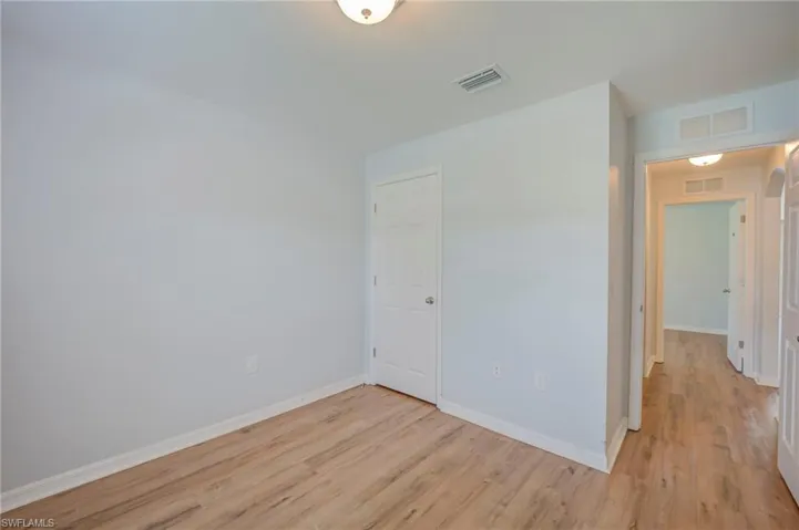 Interior room featuring light-toned walls, wood-finish flooring, a flush-mount ceiling light fixture, and a white paneled door