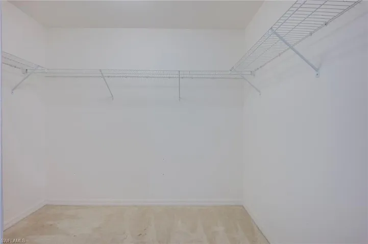 Walk-in storage space featuring neutral carpeting and tiered white wire shelving