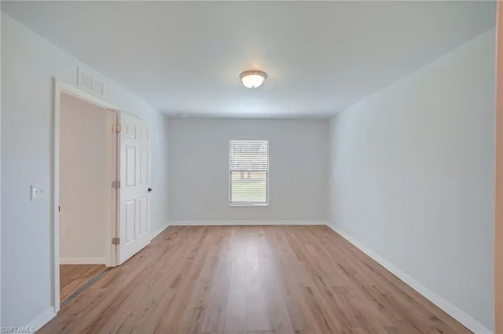 Interior space featuring neutral wall paint, wood-finish flooring, a six-panel door, and a single-hung window with blinds