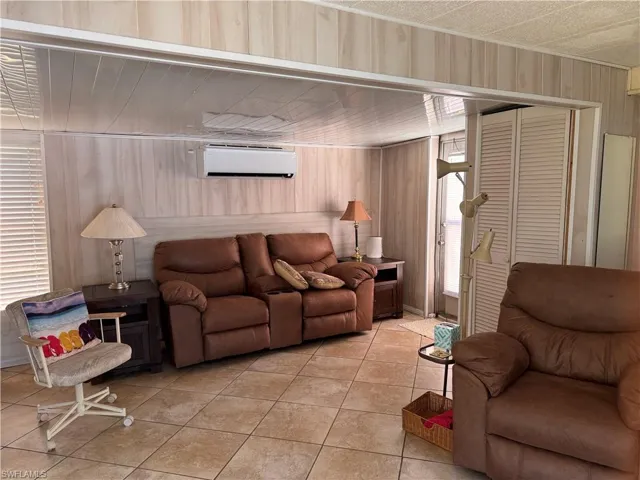 Living room featuring light tile patterned floors, wood walls, and a wall mounted AC