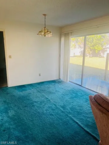 Empty room with carpet flooring, a chandelier, and a textured ceiling