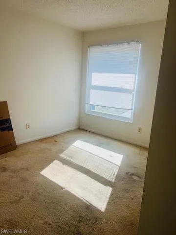 Empty room with light carpet and a textured ceiling