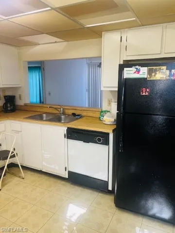Kitchen with black refrigerator, sink, white cabinets, and dishwasher