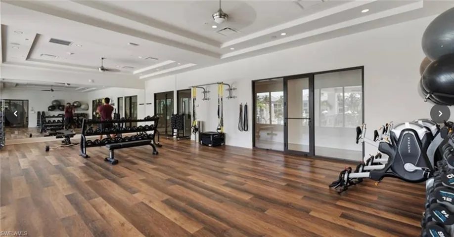 Workout area featuring a tray ceiling, dark wood-type flooring, and ceiling fan