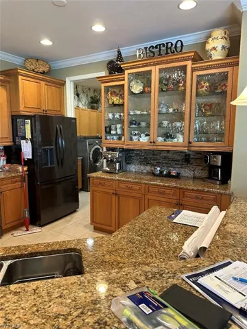 Kitchen with washer / clothes dryer, tasteful backsplash, black fridge with ice dispenser, light tile patterned floors, and crown molding