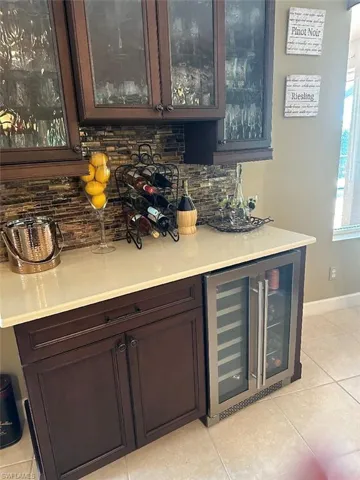 Bar with dark brown cabinetry, beverage cooler, tasteful backsplash, and light tile patterned flooring
