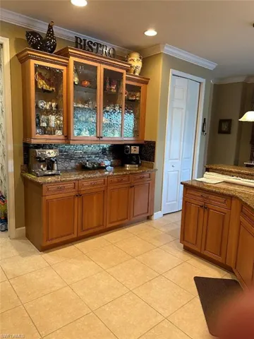 Kitchen featuring dark stone counters, backsplash, light tile patterned flooring, and crown molding
