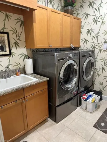Clothes washing area with cabinets, sink, independent washer and dryer, and light tile patterned flooring
