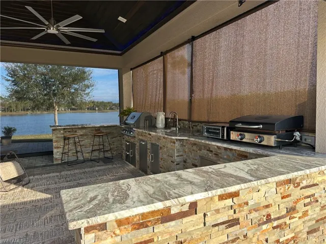 View of patio with ceiling fan, area for grilling, a water view, and an outdoor kitchen