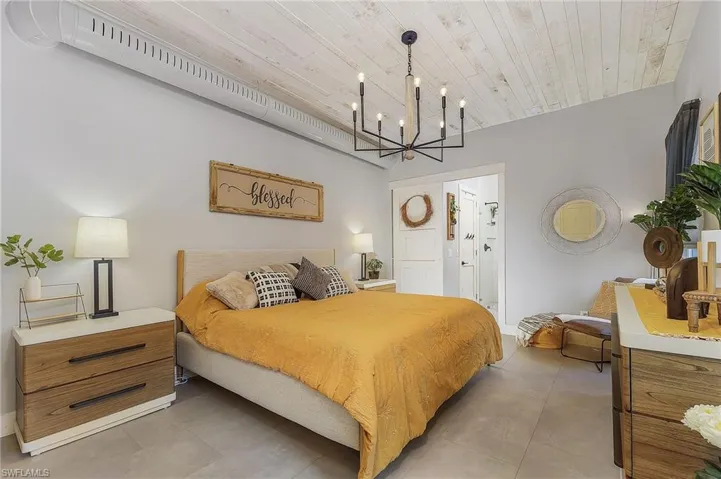 Bedroom with tile patterned floors, connected bathroom, a chandelier, and wood ceiling