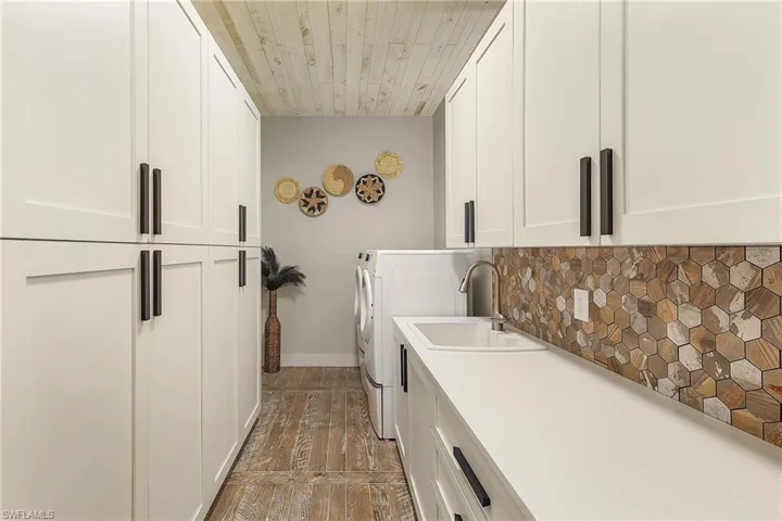 Washroom with cabinets, wood-type flooring, washing machine and dryer, and sink