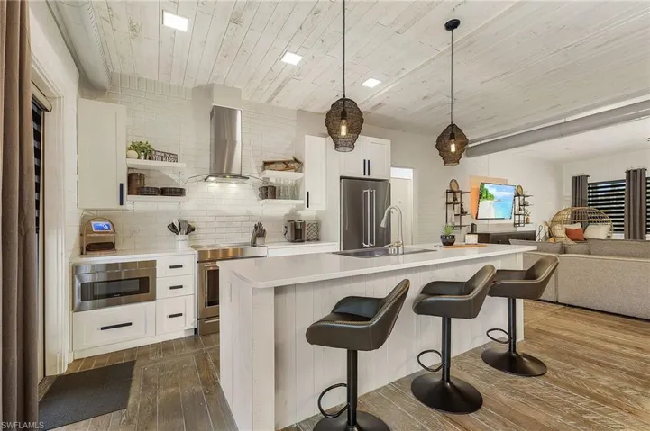 Kitchen with white cabinetry, wall chimney exhaust hood, sink, appliances with stainless steel finishes, and backsplash