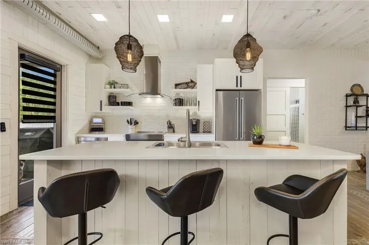 Kitchen featuring wall chimney exhaust hood, high end fridge, and an island with sink