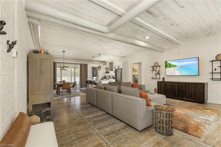 Living room featuring dark wood-type flooring, beamed ceiling, and brick wall