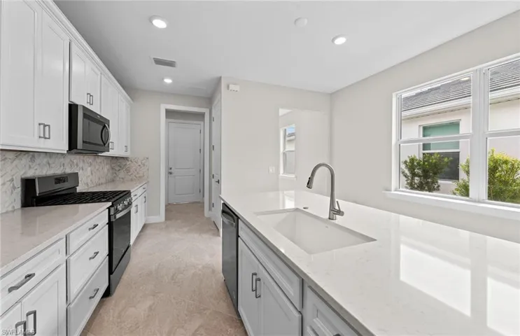 Kitchen featuring appliances with stainless steel finishes, white cabinetry, light stone counters, backsplash, and sink