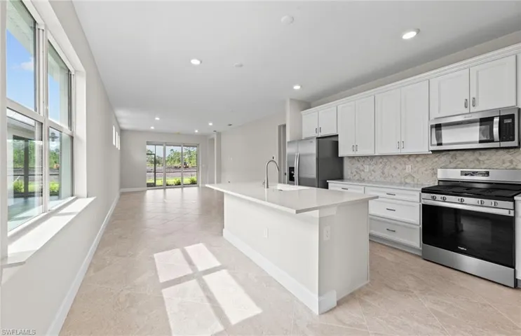Kitchen with decorative backsplash, white cabinets, stainless steel appliances, a kitchen island with sink, and sink