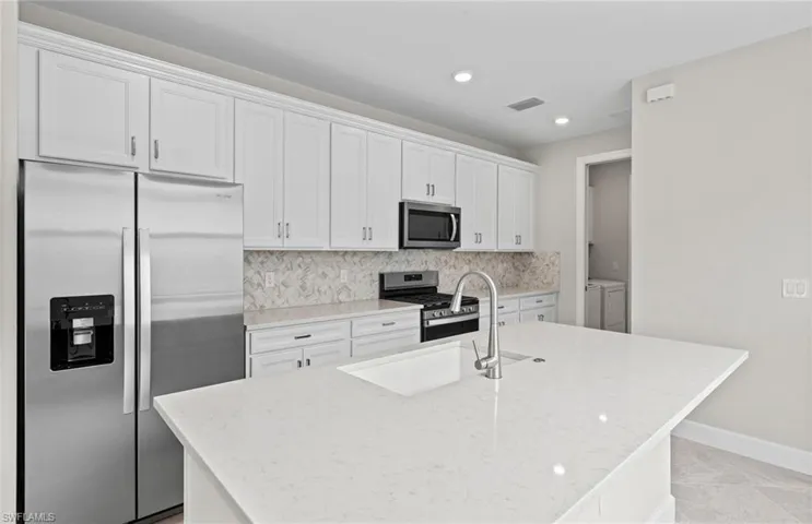 Kitchen featuring an island with sink, white cabinetry, stainless steel appliances, backsplash, and separate washer and dryer