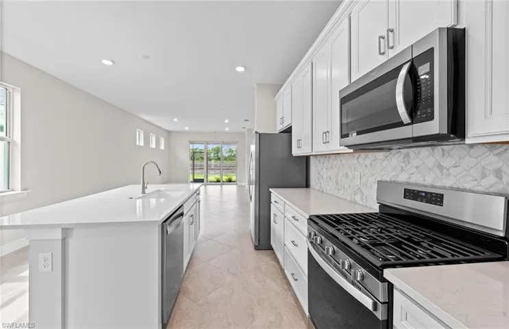 Kitchen featuring an island with sink, sink, backsplash, white cabinetry, and stainless steel appliances
