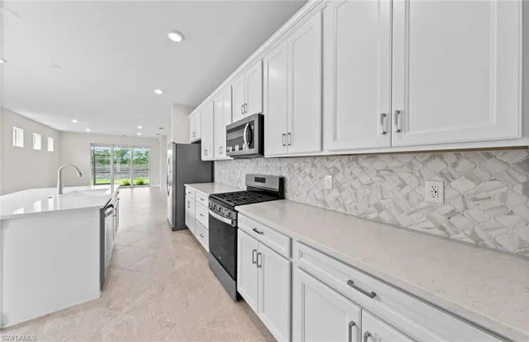 Kitchen with sink, white cabinetry, stainless steel appliances, backsplash, and light stone countertops