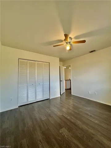 Unfurnished bedroom with a ceiling fan, a closet, and dark wood-style floors