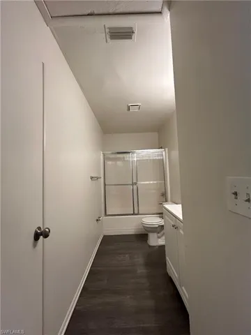 Bathroom with vanity, dark wood-style floors, and shower / bath combination with glass door