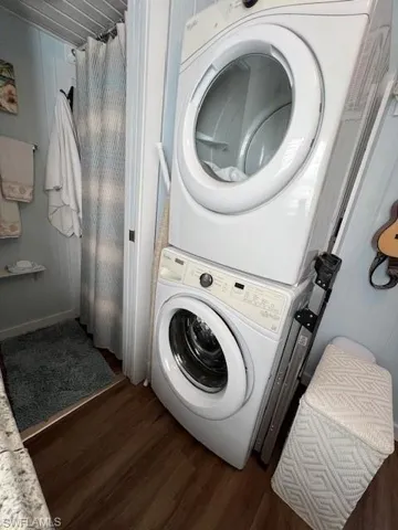 Clothes washing area with dark hardwood / wood-style flooring and stacked washer and clothes dryer