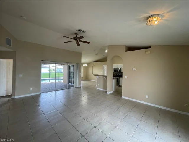 Unfurnished living room featuring light tile patterned floors, ceiling fan, arched walkways, high vaulted ceiling, and a chandelier