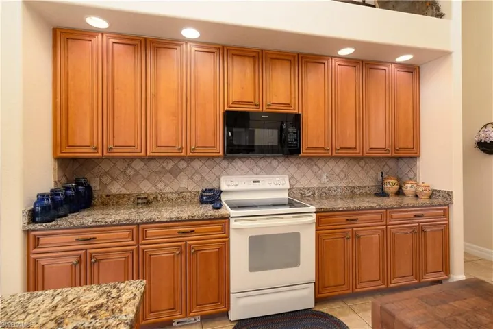 Kitchen featuring white electric range, tasteful backsplash, light tile patterned floors, and light stone counters