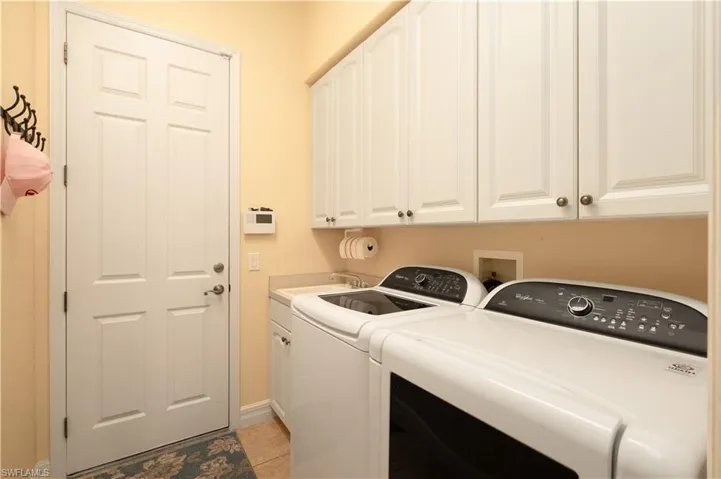 Clothes washing area featuring light tile patterned flooring, sink, separate washer and dryer, and cabinets