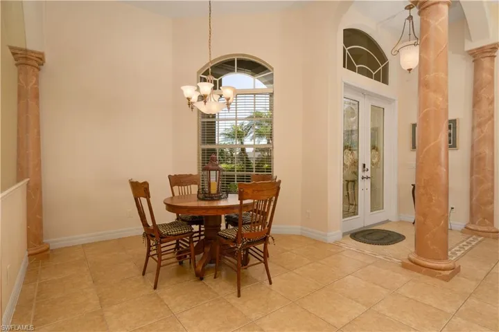 Tiled dining space with a chandelier, a towering ceiling, french doors, and ornate columns