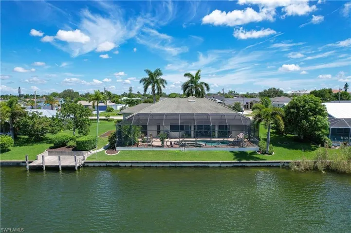 Back of property with glass enclosure, a water view, and a lawn