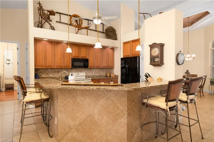 Kitchen featuring light hardwood / wood-style flooring, black appliances, decorative light fixtures, dark stone countertops, and ceiling fan