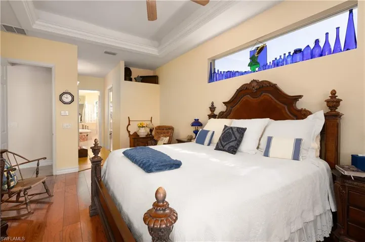 Bedroom with connected bathroom, ceiling fan, hardwood / wood-style floors, and a tray ceiling