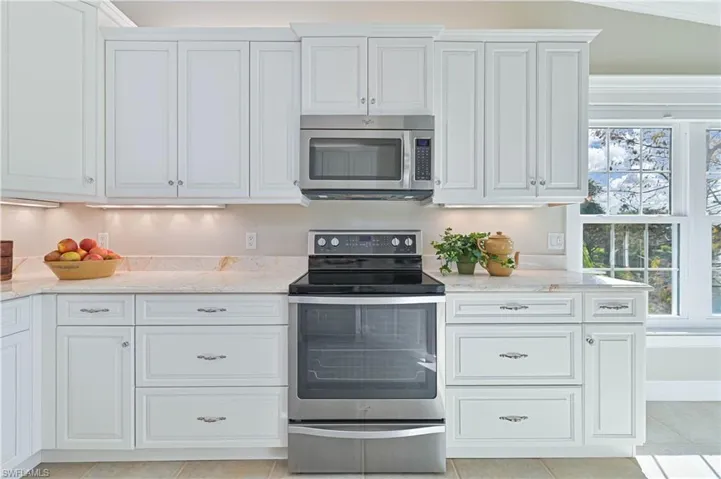 Kitchen featuring stainless steel appliances, light stone counters, and white cabinetry