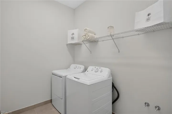 Dedicated laundry area with light gray walls, neutral-toned floor tiling, and a wire shelving system